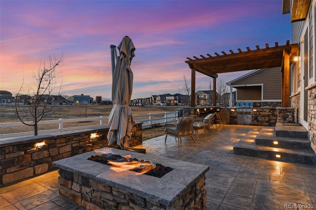 patio terrace at dusk with a pergola, an outdoor fire pit, and area for grilling