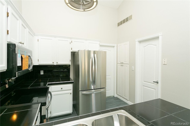 kitchen featuring tile countertops, stainless steel appliances, visible vents, white cabinetry, and tasteful backsplash