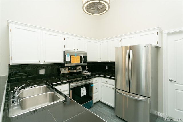 kitchen featuring tile countertops, a sink, white cabinetry, appliances with stainless steel finishes, and tasteful backsplash