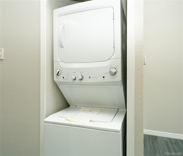 laundry area with stacked washer and dryer, laundry area, baseboards, a textured wall, and wood finished floors