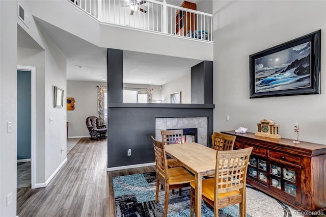 dining room with visible vents, baseboards, wood finished floors, a high ceiling, and a tile fireplace