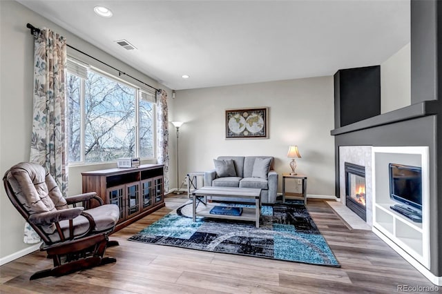 living room with a tiled fireplace, visible vents, recessed lighting, baseboards, and wood finished floors
