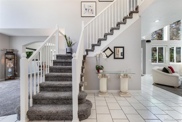 stairs with a towering ceiling, tile patterned flooring, and baseboards