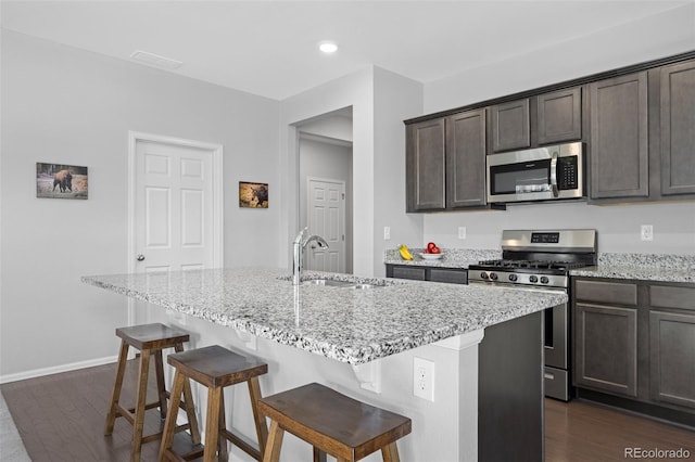 kitchen featuring light stone counters, dark wood-style floors, stainless steel appliances, and a sink