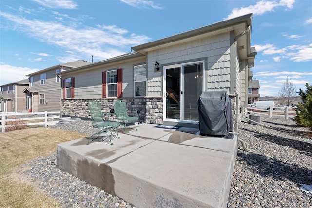 view of front of home with a patio area, fence, and stone siding