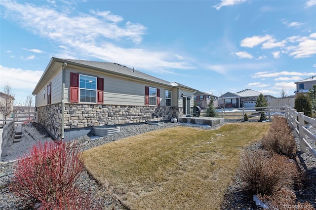 back of property with a yard, stone siding, and fence