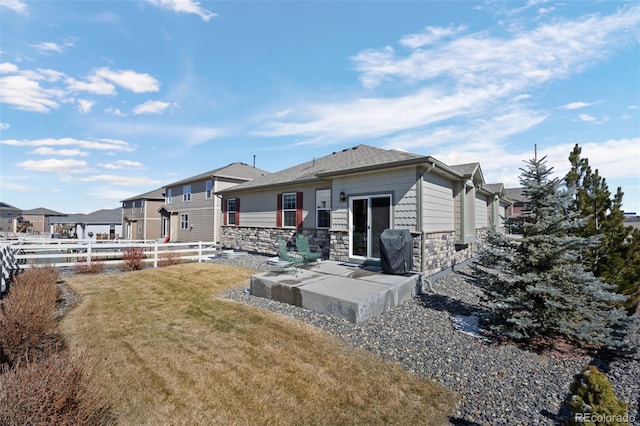 rear view of house with stone siding, a lawn, fence, and a patio area