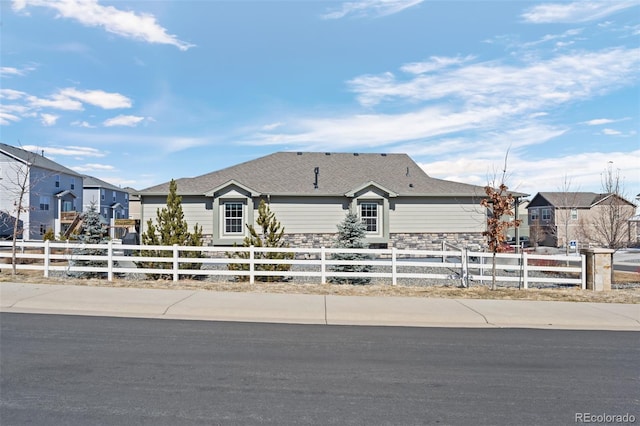 single story home with a fenced front yard, stone siding, a residential view, and a shingled roof