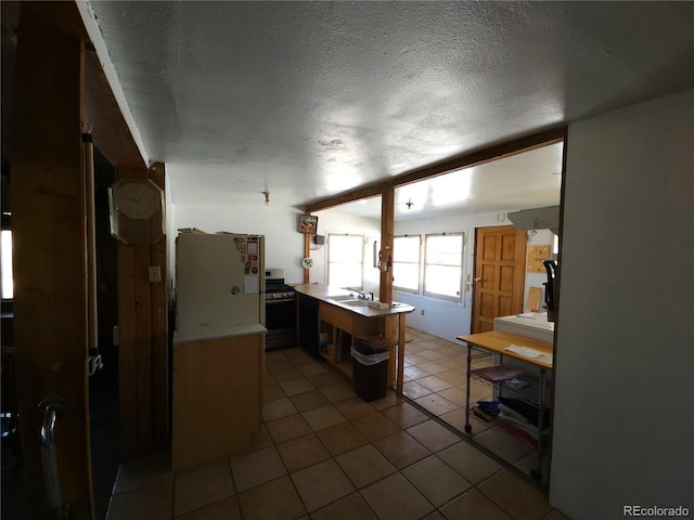 kitchen featuring kitchen peninsula, sink, light tile patterned floors, stainless steel range, and a textured ceiling