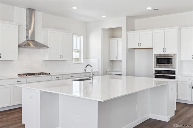 kitchen with wall chimney exhaust hood, sink, white cabinetry, a center island with sink, and stainless steel appliances