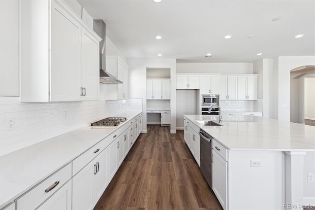 kitchen with appliances with stainless steel finishes, white cabinetry, sink, a kitchen island with sink, and wall chimney exhaust hood