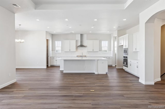 kitchen with appliances with stainless steel finishes, a wealth of natural light, wall chimney range hood, a kitchen island with sink, and white cabinets