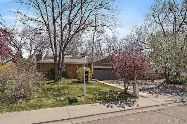 view of front of house featuring concrete driveway, a chimney, a front yard, brick siding, and a garage
