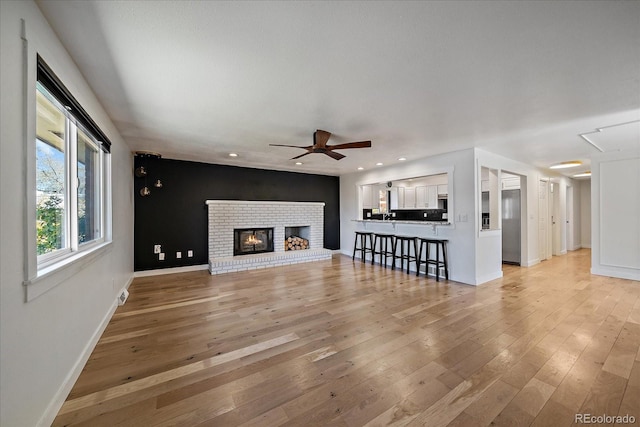 unfurnished living room with light wood-style floors, ceiling fan, a fireplace, recessed lighting, and baseboards