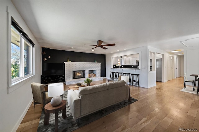 living room with light wood-type flooring, baseboards, recessed lighting, a fireplace, and ceiling fan