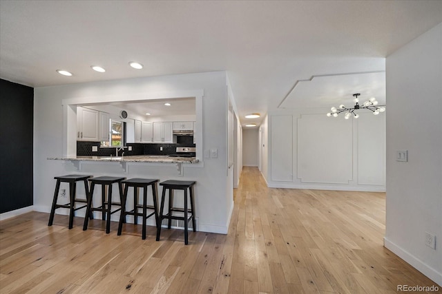 kitchen featuring stainless steel range oven, light wood-type flooring, a chandelier, under cabinet range hood, and white cabinetry