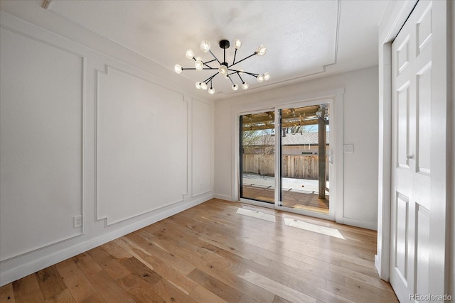 unfurnished dining area with light wood-type flooring, an inviting chandelier, and baseboards