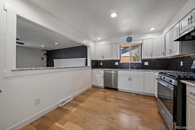 kitchen with visible vents, a sink, light wood-style floors, stainless steel appliances, and backsplash