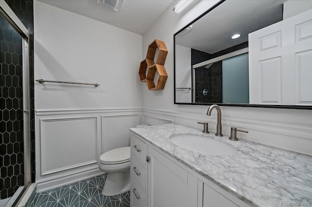 bathroom featuring a decorative wall, toilet, wainscoting, vanity, and a stall shower