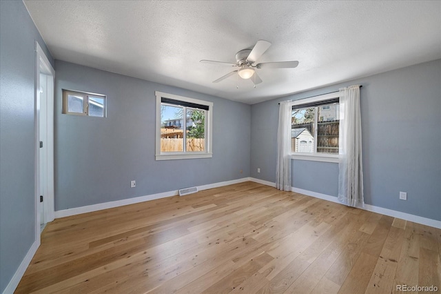 unfurnished room featuring baseboards, light wood-type flooring, a textured ceiling, a ceiling fan, and visible vents