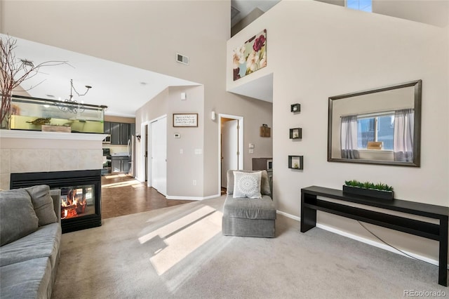 carpeted living room with a tiled fireplace and a high ceiling