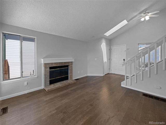 unfurnished living room with a textured ceiling, lofted ceiling with skylight, ceiling fan, dark wood-type flooring, and a fireplace