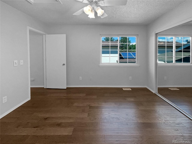 unfurnished room featuring ceiling fan, dark wood-type flooring, a healthy amount of sunlight, and a textured ceiling