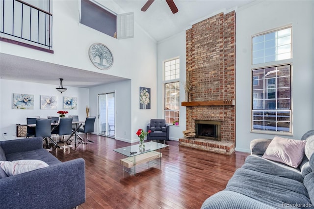 living area featuring baseboards, a ceiling fan, wood-type flooring, a brick fireplace, and high vaulted ceiling