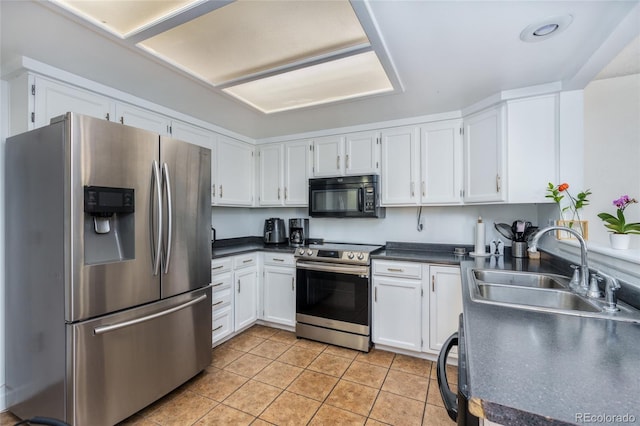 kitchen featuring light tile patterned floors, stainless steel appliances, a sink, white cabinetry, and dark countertops