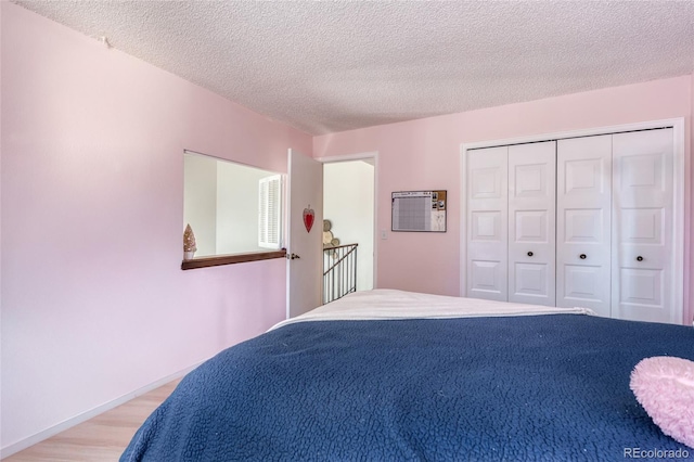 bedroom with light wood finished floors, a closet, baseboards, and a textured ceiling