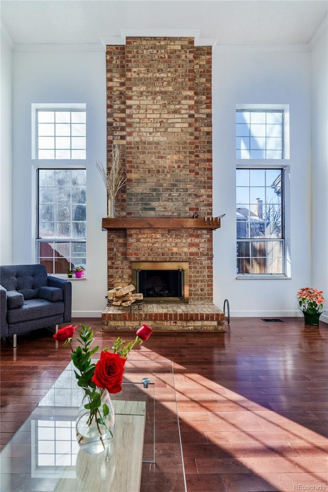 living area with a high ceiling, a fireplace, visible vents, ornamental molding, and wood-type flooring