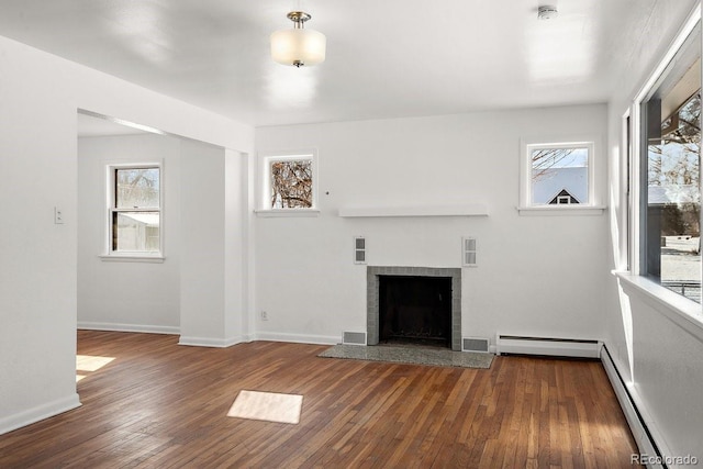 unfurnished living room with dark wood-type flooring, a wealth of natural light, and a baseboard heating unit