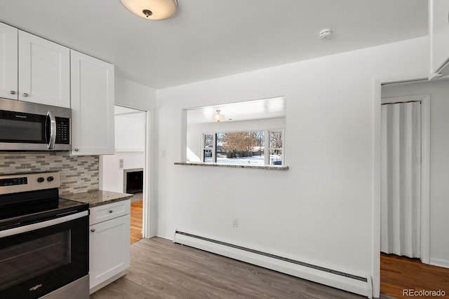 kitchen with white cabinetry, a baseboard heating unit, dark stone counters, and appliances with stainless steel finishes