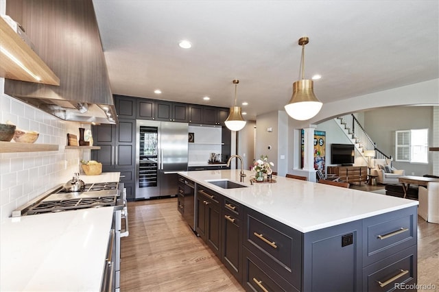 kitchen with range hood, arched walkways, appliances with stainless steel finishes, light countertops, and a sink