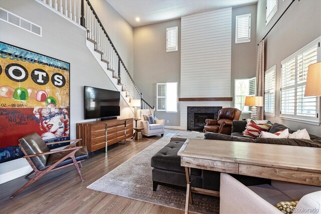 living room featuring a fireplace, visible vents, a high ceiling, and wood finished floors