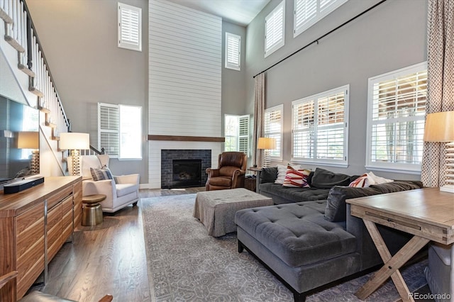 living area featuring a fireplace with flush hearth, wood finished floors, a towering ceiling, and plenty of natural light
