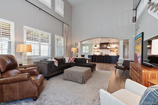 living area with decorative columns, arched walkways, a high ceiling, and wood finished floors
