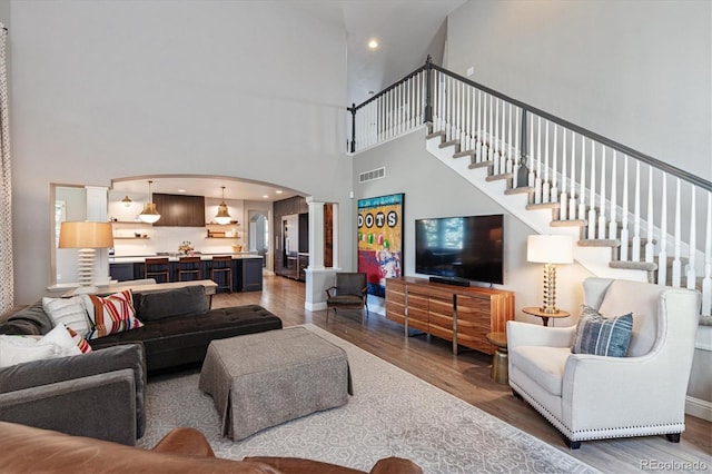 living area with ornate columns, arched walkways, visible vents, wood finished floors, and a high ceiling