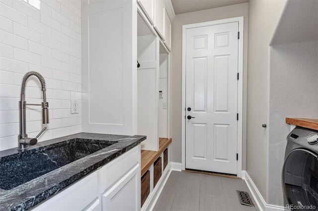 laundry area featuring washer / clothes dryer, visible vents, a sink, baseboards, and cabinet space