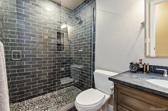 bathroom featuring toilet, a stall shower, vanity, and a textured wall