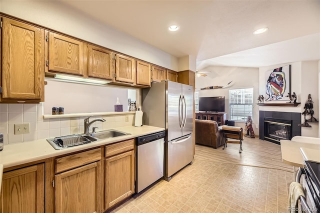 kitchen featuring sink, ceiling fan, stainless steel appliances, a fireplace, and decorative backsplash