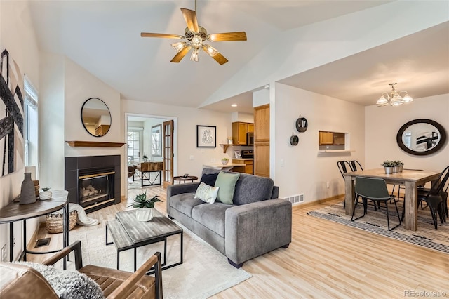 living room with a tiled fireplace, light wood finished floors, baseboards, ceiling fan with notable chandelier, and visible vents