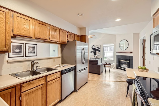 kitchen featuring light countertops, a fireplace, tasteful backsplash, appliances with stainless steel finishes, and a sink