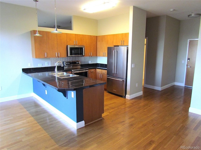 kitchen with wood finished floors, brown cabinetry, a peninsula, a sink, and appliances with stainless steel finishes