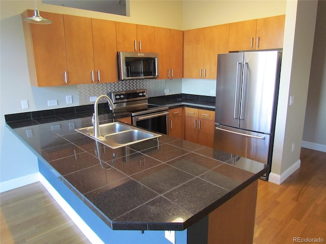 kitchen with baseboards, a peninsula, light wood-style flooring, a sink, and stainless steel appliances