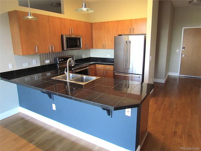 kitchen with tile counters, pendant lighting, appliances with stainless steel finishes, a peninsula, and dark wood-style flooring