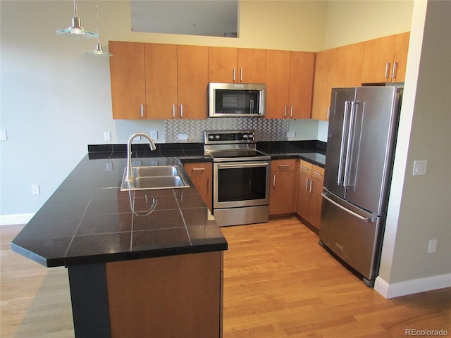 kitchen featuring a sink, backsplash, light wood-style floors, appliances with stainless steel finishes, and a peninsula