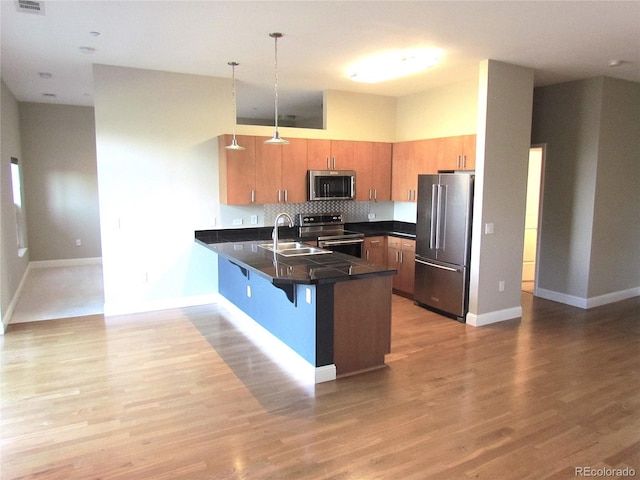 kitchen with light wood finished floors, a breakfast bar area, a peninsula, stainless steel appliances, and a sink