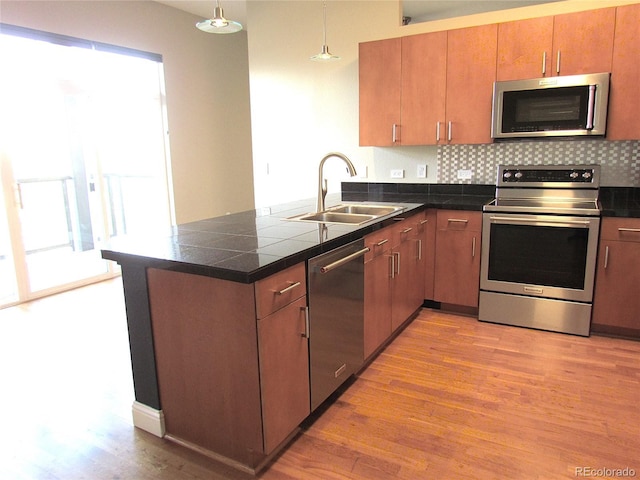 kitchen featuring a peninsula, light wood-style floors, hanging light fixtures, stainless steel appliances, and a sink