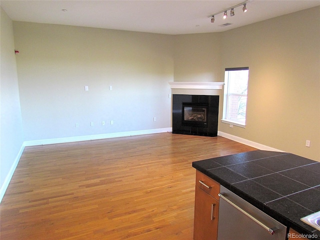 unfurnished living room featuring track lighting, light wood-style flooring, baseboards, and a tile fireplace